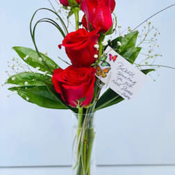 Red roses arranged in a clear glass vase with greenery