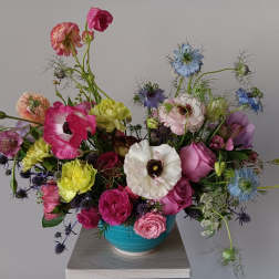Colorful mixed bouquet in a turquoise vase with pink, white, blue, and yellow blooms