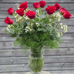 Red roses arranged in a clear glass vase with white filler flowers