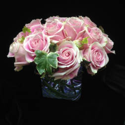Low arrangement of pink roses with ivy accents in a clear glass cube vase