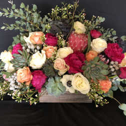 Low floral arrangement with roses, protea, and succulents in a wooden box