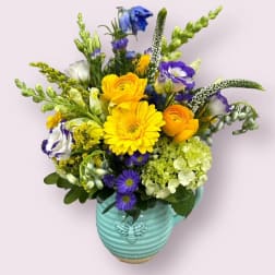 Mixed bouquet in a turquoise vase with yellow, purple, white, and green blooms