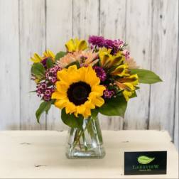 Sunflower bouquet with purple and peach flowers in a clear glass vase