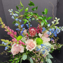 Pink roses and blue flowers arranged in a black container with a leafy arch