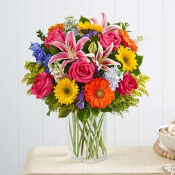 Mixed bouquet of pink roses, lilies, and bright daisies in a clear glass vase