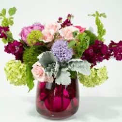 Mixed bouquet in a magenta glass vase with pink, purple, and green blooms