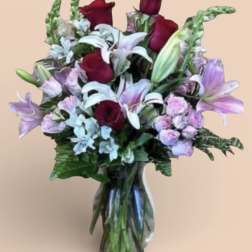 Bouquet of red roses, white lilies, and lavender flowers in a glass vase