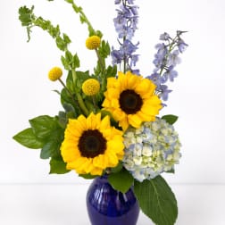 Sunny bouquet with sunflowers, blue hydrangea, delphinium and Bells of Ireland in a cobalt glass vase