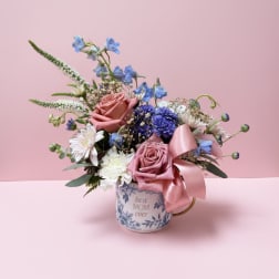 Mixed pink and blue flower arrangement in a floral mug with a ribbon