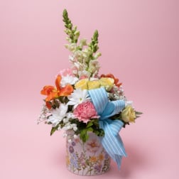 Mixed flower arrangement in a floral tin with a blue ribbon