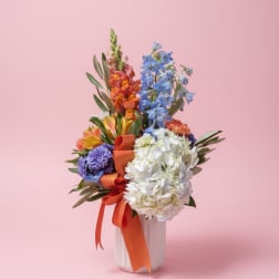 Colorful mixed bouquet in a white vase with orange ribbon