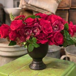 Red rose arrangement with orchids in a dark vase