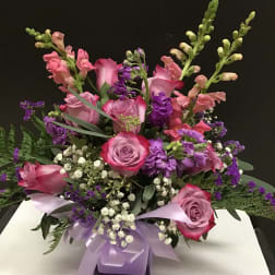 Pink and purple floral arrangement with roses and snapdragons in a ribbon-tied vase