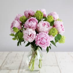 Pink peonies and green blooms in a clear glass vase