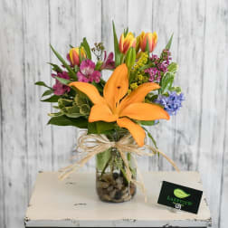 Mixed bouquet with orange lily and colorful tulips in a glass vase