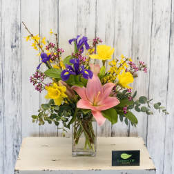Mixed bouquet with pink lily, yellow daffodils, and purple iris in a glass vase