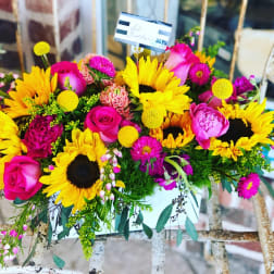 Bright bouquet with sunflowers, pink roses, and magenta flowers in a white container