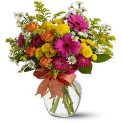 Mixed bouquet of pink, yellow, orange, and white flowers in a clear glass vase