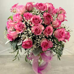 Pink roses arranged in a glass vase with baby's breath and ribbon