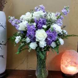 White roses and purple flowers arranged in a glass vase