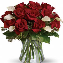 Red roses and white calla lilies in a clear glass vase