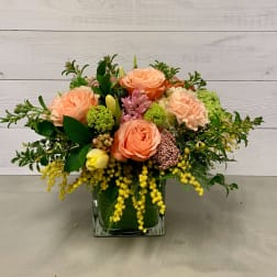 Peach roses and mixed blooms arranged in a square glass vase