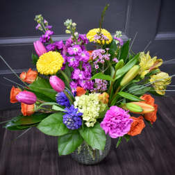 Colorful mixed bouquet in a glass vase with tulips, roses, lilies, and mums