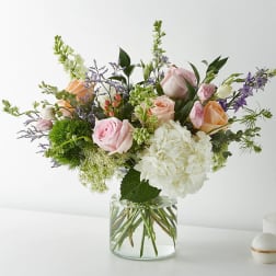 Mixed bouquet of pink and peach roses with white hydrangea in a glass vase