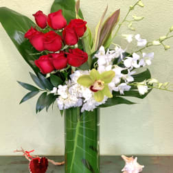 Red roses and white orchids arranged in a tall glass vase
