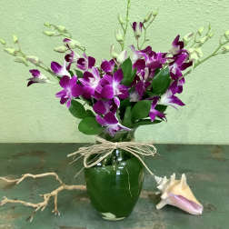 Purple orchids arranged in a green glass vase with a raffia bow