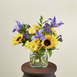 Yellow sunflowers and purple flowers in a clear glass vase