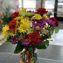 Colorful bouquet of daisies and carnations in a glass vase with ribbon curls