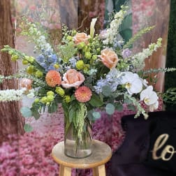 Tall mixed bouquet in a clear glass vase with peach roses and white orchids