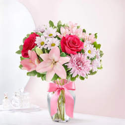 Pink and white mixed flower bouquet in a glass vase with a pink ribbon