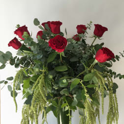 Tall bouquet of red roses with cascading green foliage in a glass vase