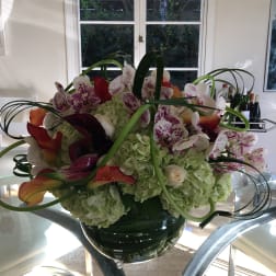 Large floral arrangement with orchids, hydrangeas, and calla lilies in a glass vase
