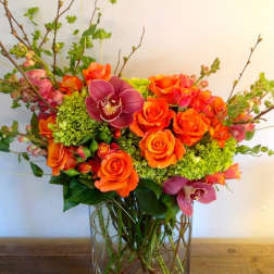 Orange roses and magenta orchids in a clear glass vase