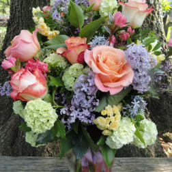 Bouquet of pink roses, lilac blooms, and pale green hydrangeas in a glass vase