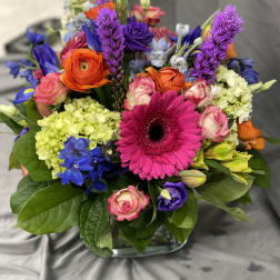 Colorful mixed bouquet with gerbera daisies, roses, and hydrangeas in a glass vase