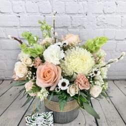 Pastel flower arrangement with roses, chrysanthemums, and daisies in a rustic container
