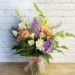 Mixed bouquet of peach roses, purple flowers, and white blooms in a glass vase