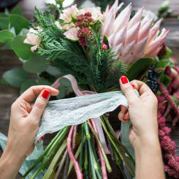 Hands tying lace around a pink and green bouquet