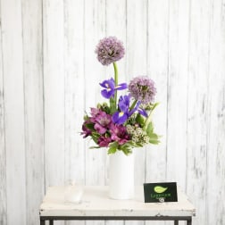 Tall modern arrangement with purple allium, blue irises, and magenta flowers in a white vase