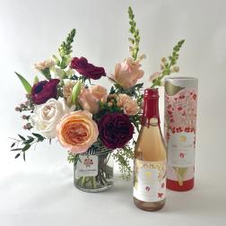 Bouquet of roses and snapdragons in a glass vase beside a bottle and gift box