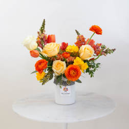 Bright mixed bouquet in a white vase with orange, yellow, and cream flowers