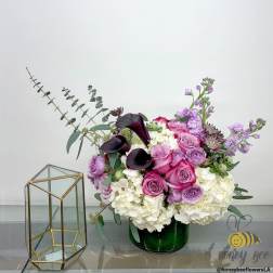 Pink and purple floral arrangement in a green vase beside a glass terrarium