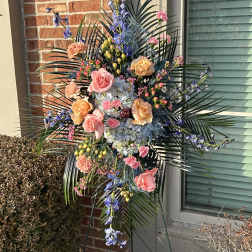 Tall standing floral spray with pink and peach roses and blue flowers