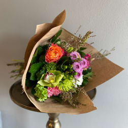 Mixed bouquet with orange, pink, and green flowers wrapped in brown paper