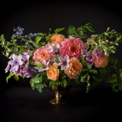 Mixed bouquet of pink, peach, and lavender flowers in a gold vase