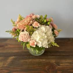 Low arrangement of white hydrangeas and peach roses, carnations, and mums in a clear glass vase
